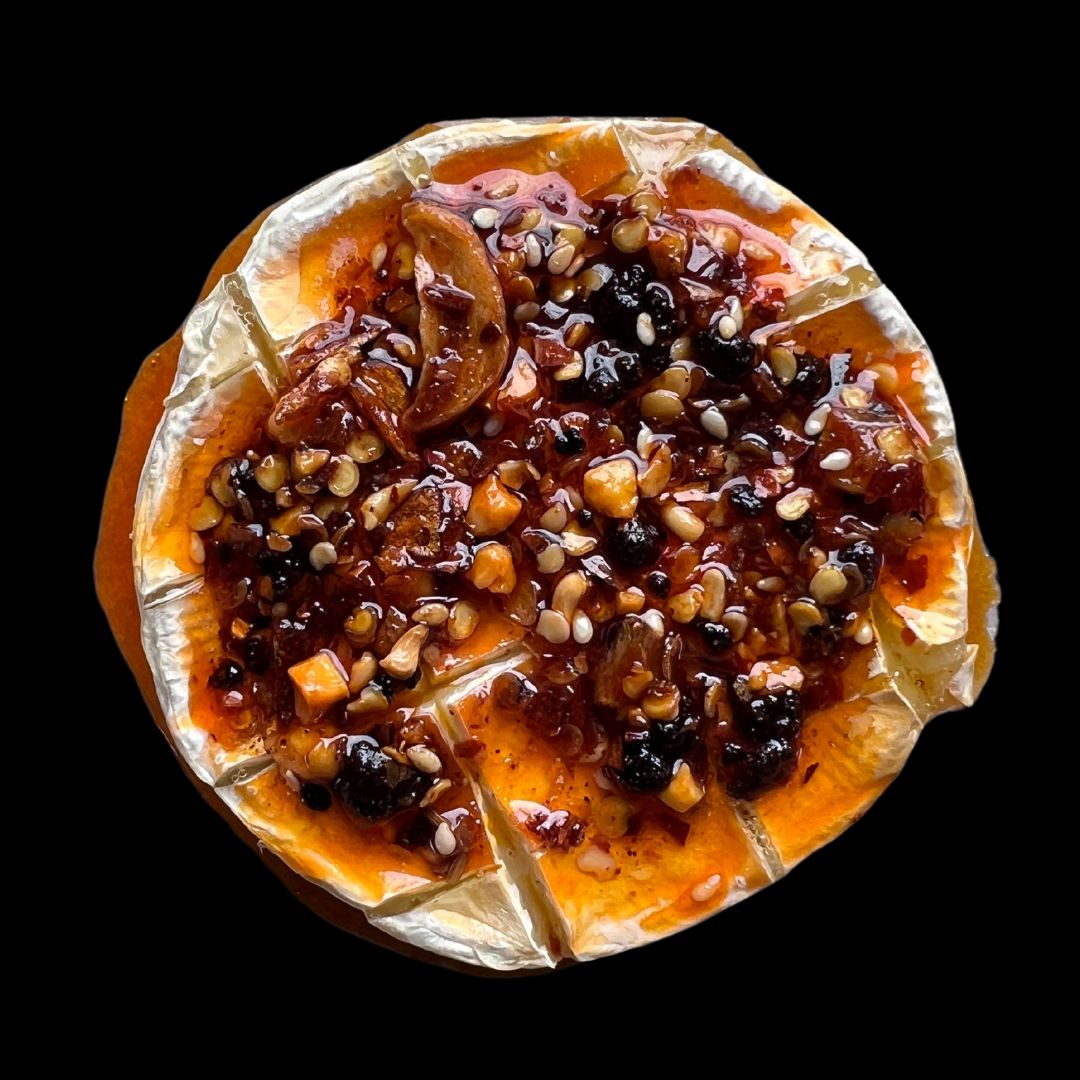 Baked brie in a cast iron pan topped with chilli crisp, with charred sourdough