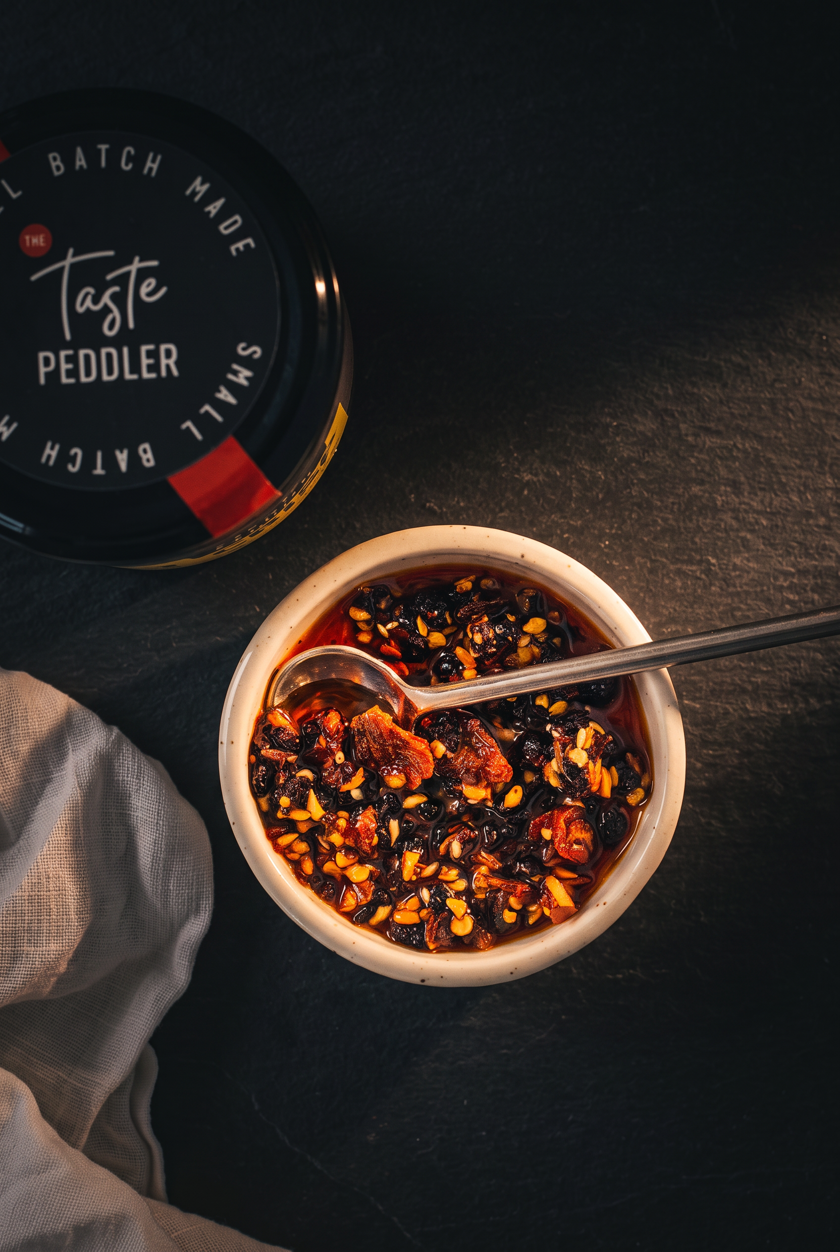 Overhead bowl of chilli crisp with a spoon beside the jar lid
